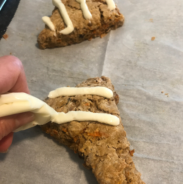 carrot cake scones being topped with cream cheese icing